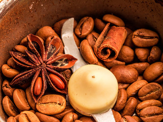 Macro photo of freshly ground coffee in electric coffee grinder with roasted coffee beans inside and coffee grains with oriental spices, anise and cinnamon close-up view of the top.