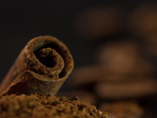 stick of cinnamon with a vintage spoon of ground coffee. coffee with spices. Food background on dark stone table. Macro close-up image.