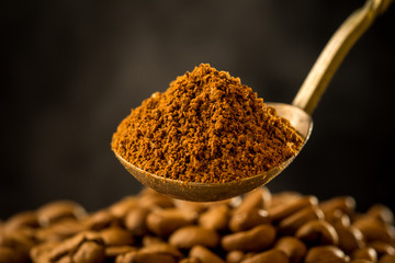 Roasted ground coffee into an old silver spoon and roasting coffee beans with smoke steam on dark background. Close-up photo. Vintage style effect picture, with copy space.