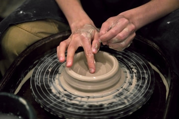 Hands in clay shape the product on a potter's wheel, close-up