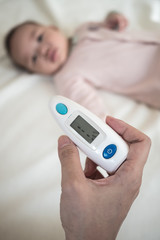 Ear Thermometer in parent hand with blurred new born baby background