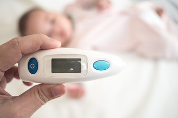 Ear Thermometer in parent hand with blurred new born baby background