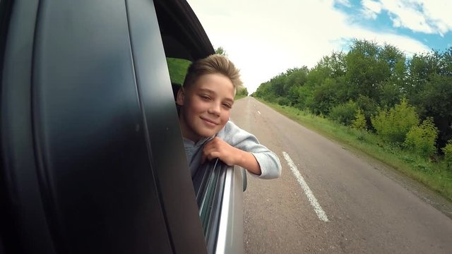 Good mood. Happy joyful teen boy rides travels on road in the car . Summer romantic adventures and trips, childhood memories and dreams. Headwind blowing in face. Slow motion