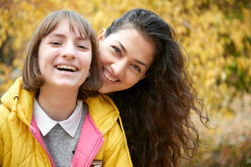 Fototapeta premium Portrait of pretty woman and teen girl. They are posing in autumn park. Beautiful landscape at fall season.