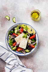 Traditional Greek Salad. Vegetarian dish with fresh lettuce, olives, peppers, cucumbers, onions and feta cheese. On light rustic concrete background. Top view.