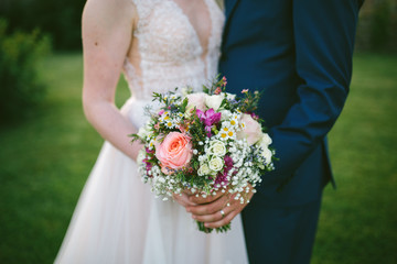 wedding couple hold bouquet with roses and camomiles