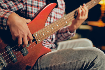 Obraz na płótnie Canvas Close up of young man playing bass guitar. Home studio interior.