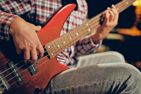 Close up of young man playing bass guitar. Home studio interior.