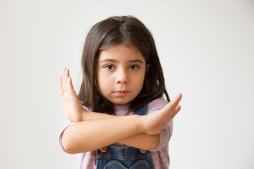 Adorable Hispanic child making stop gesture. Little serious girl gesturing forbidden. Isolated on white. Prohibition concept