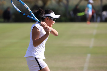天然芝のコートでバックハンドストロークを打つジュニアテニスプレイヤー
