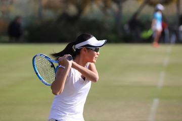 天然芝のコートでバックハンドストロークを打つジュニアテニスプレイヤー