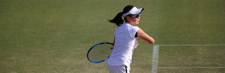 天然芝のコートでレシーブを打つジュニアテニスプレイヤー