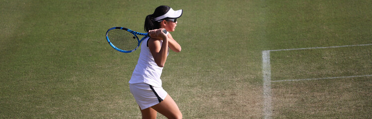 天然芝のコートでレシーブを打つジュニアテニスプレイヤー