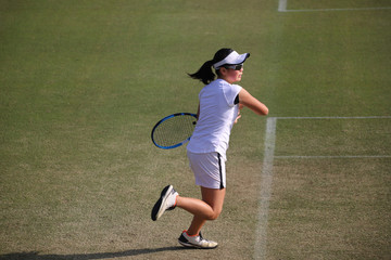 天然芝のコートでフォアハンドストロークを打つジュニアテニスプレイヤー