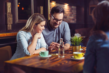 Young happy couple having coffee in cafe and looking at phone.