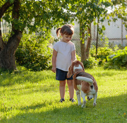 Happy little girl with dog in sunny summer day in garden.