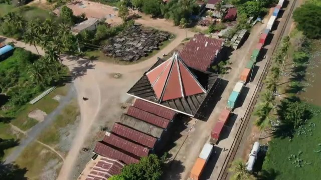 Aerial drone view flying towards a vintage colonial era train station in rural Cambodia, Southeast Asia; camera settles above old station building with downward view.