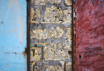 Blue and red painted metal doors in a brick and concrete rough wall forming a grungy abstract texture background
