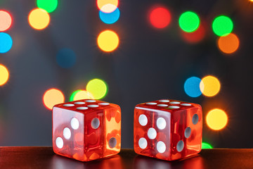 Two red glass dice on a polished wooden table on bokeh background of multi-colored lights. Festive win concept. Six and six.