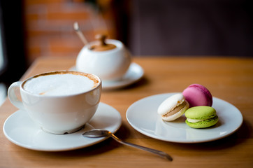 Cappuccino coffee in white cup with colorful macaroons served on wooden table