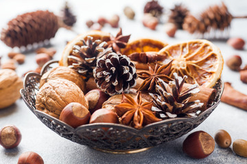 Winter food ingredients nuts cones oranges cinnamon star anise in a bowl. Rustic style.