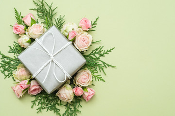 present gift box in silver paper and bunch of roses and twigs composition on light green background.