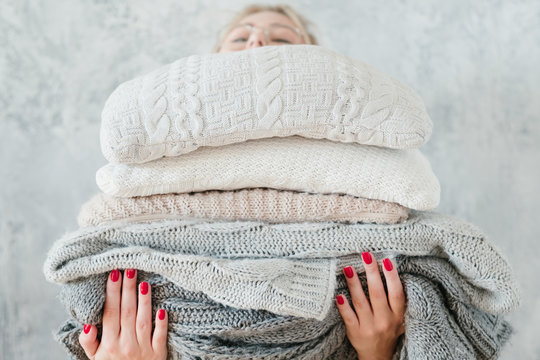 woman holding big stack of knitted plaids and blankets. cozy and warm winter home decor