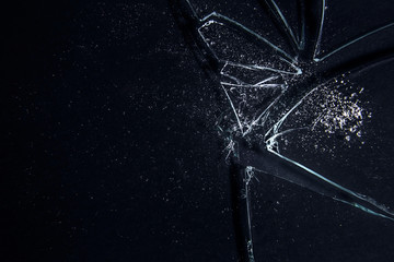 A broken glass on a black surface, with many sharp shards creating a white irregular textured...