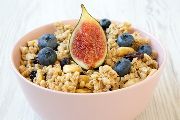 Fruit granola in pink bowl on a white wooden table, side view. Close-up.