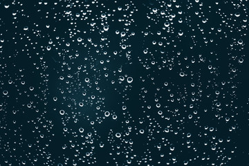 Fototapeta na wymiar Dirty window glass with drops of rain. Atmospheric blue background with raindrops. Droplets and stains close up. Detailed transparent texture in macro with copy space. Rainy weather.