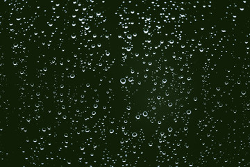 Fototapeta na wymiar Dirty window glass with drops of rain. Atmospheric green background with raindrops. Droplets and stains close up. Detailed transparent texture in macro with copy space. Rainy weather.