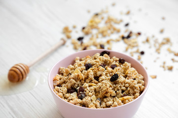 Pink bowl of fruit granola and honey over white wooden background, side view. Close-up.