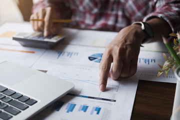 Close up of businessman or accountant hand holding pen working on calculator to calculate business data, accountancy document and laptop computer at office, business concept