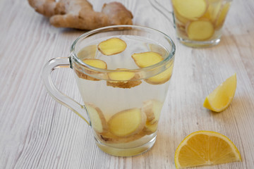 A mug of homemade ginger tea with lemon on white wooden surface, side view.