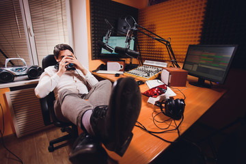 Portrait of handsome young latin man sitting in front of a microphone with laptop at radio station.