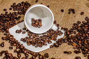 Coffee beans in a white cup lying on a side on a background of hessian