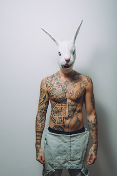 Portrait of young man with wearing rabbit mask, bare chest covered in tattoos