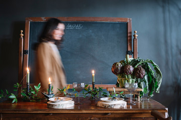 Young woman moving past vintage dinner table with candles and bowl of globe artichokes