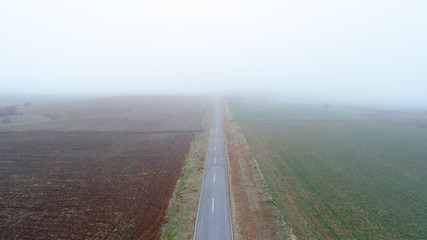 Aerial view on  speed road, partly covered by fog. Vertical view on rural countryside in autumn, foggy morning. Misty empty road.
