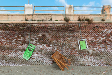 Beach chairs and wooden table, hanging from a red brick wall with a chain and padlock, it is...