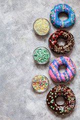 homemade doughnuts with colored frosting and different sprinkles on a gray background