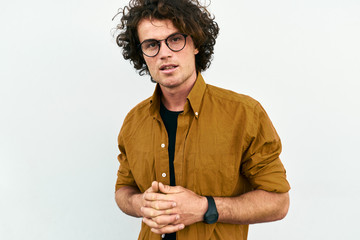 Fototapeta na wymiar Horizontal portrait of handsome smart man with curly hair, wears spectacles posing for social advertisement, isolated on white wall with copy space for your promotional information.