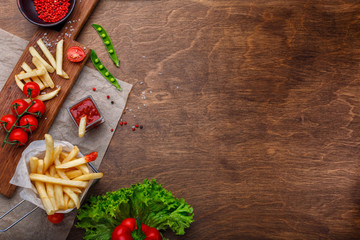 French fries in a grid with ketchup, salad and cherry tomatoes on wooden brown table