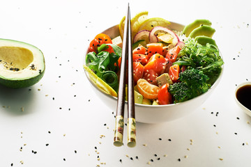poke bowl with salmon, avocado, cucumbers, arugula, broccoli, rice, carrots, cheese and chukha with chopsticks and soy sauce isolated over white background. top view