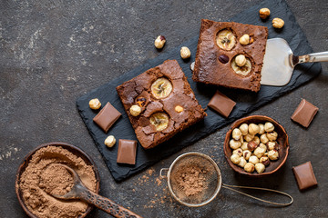 brownie with banana and hazelnut on black slate plates on dark background