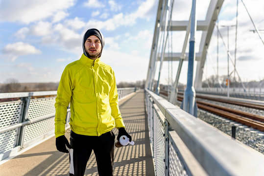 Portrait of young athlete man in windbreaker preparing to exercise on sunny winter day