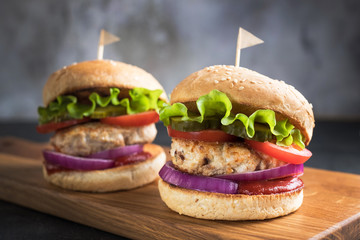 Two homemade turkey burgers with salad, tomatoes, pickles and red onion on wooden cutting board