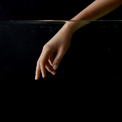 partial view of girl putting hand into clear water isolated on black