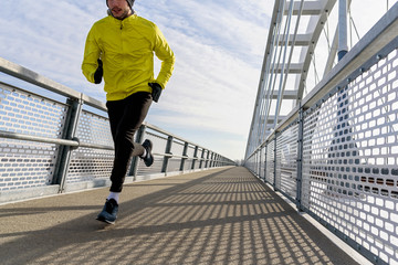 Attractive fit man running fast along big modern bridge. Exercising, Jogging, Sport, Winter. Male athlete running.