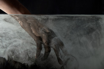 cropped view of person putting hand into water with dark paint